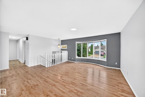 Spacious interior featuring wood-finish flooring, a curved bay window, and a white baluster staircase - 1103 56 Street, Edmonton, AB 
