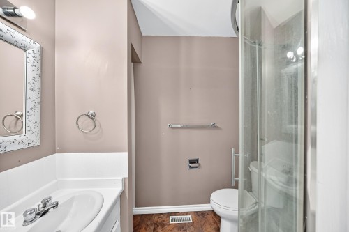 Bathroom featuring a white vanity with integrated sink, chrome faucet, mirrored medicine cabinet with decorative frame, glass-enclosed shower, and wood-finish flooring - 1103 56 Street, Edmonton, AB 