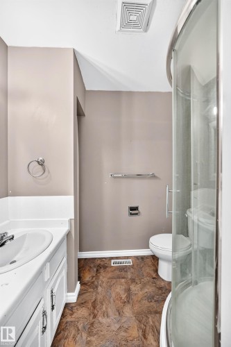 Bathroom featuring a white vanity with an integrated sink, a curved glass shower enclosure, and brown-toned tile flooring - 1103 56 Street, Edmonton, AB 