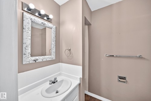 Bathroom vanity featuring an integrated sink, white countertop, and decorative framed mirror - 1103 56 Street, Edmonton, AB 