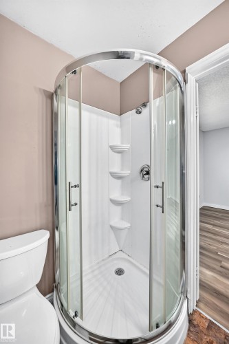 Corner shower enclosure with clear glass doors, chrome hardware, integrated shelving, and a white base - 1103 56 Street, Edmonton, AB 