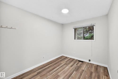 Room featuring wood-finish flooring, a single window with horizontal blinds, and a flush-mount ceiling light fixture - 1103 56 Street, Edmonton, AB 
