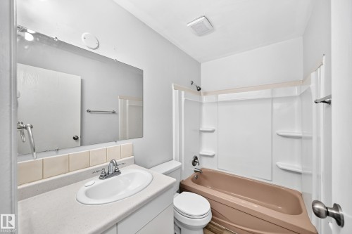Bathroom featuring a built-in vanity with an integrated sink and chrome faucet, a mounted mirror, and a full bathtub with shower surround - 1103 56 Street, Edmonton, AB 