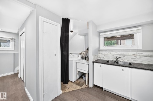Utility area featuring a double basin sink with dark countertop, white base cabinetry, and a textured tile backsplash - 1103 56 Street, Edmonton, AB 