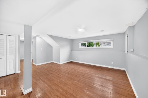 Spacious interior room featuring wood-finish flooring, light gray wall paint, and white baseboards - 1103 56 Street, Edmonton, AB 
