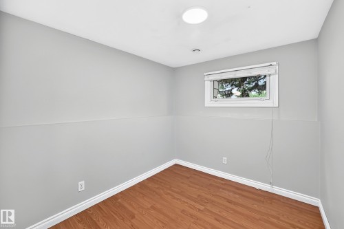 Interior room featuring light gray walls, white baseboards, wood-finish flooring, and a large window with white trim - 1103 56 Street, Edmonton, AB 