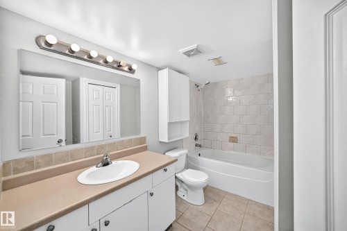 Bathroom featuring an integrated bathtub and shower with subway tile surround, tile flooring, an elongated vanity with an integrated sink, and a wall-mounted medicine cabinet - 1103 56 Street, Edmonton, AB 