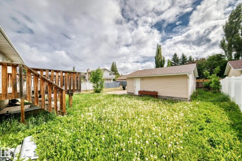 Expansive backyard featuring a wood deck with railings, a detached garage with beige siding and a shingle roof, and a white picket fence bordering the property - 1103 56 Street, Edmonton, AB 