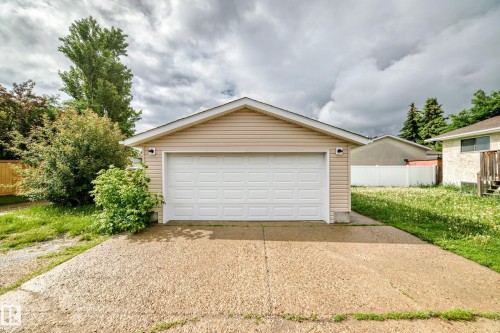 Detached garage with tan siding, a white panel garage door, and a concrete driveway - 1103 56 Street, Edmonton, AB 