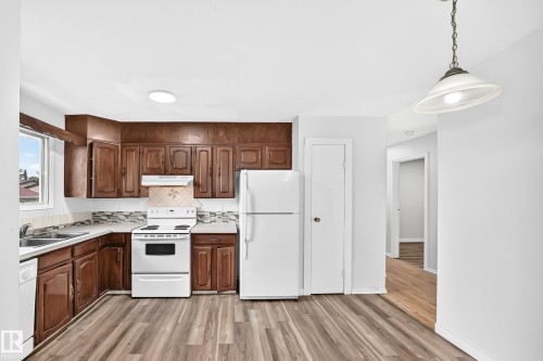 Kitchen with wood-finish flooring, wood cabinetry, white appliances, and a tiled backsplash - 1103 56 Street, Edmonton, AB 