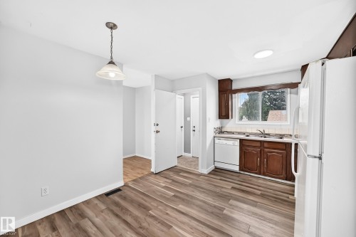 Kitchen featuring wood-finish flooring, dark wood cabinetry, a white tile backsplash, and a window above the sink - 1103 56 Street, Edmonton, AB 