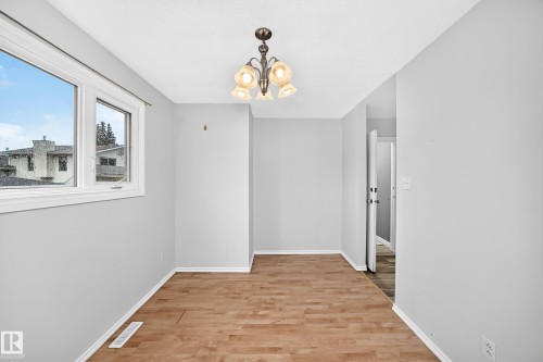 Neutral-toned interior featuring wood-finish flooring, a multi-pane window, and a decorative ceiling fixture - 1103 56 Street, Edmonton, AB 