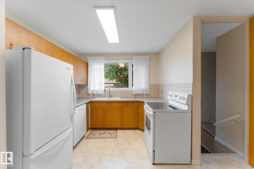 Kitchen featuring wood-finish cabinetry, a window with natural light, tiled backsplash, and a built-in sink - 15112 76A Avenue, Edmonton, AB 