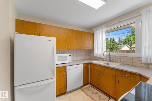 Kitchen featuring wood-finish cabinetry, light-toned countertops, and a white tile backsplash - 15112 76A Avenue, Edmonton, AB 