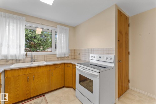 Kitchen featuring wood-finish cabinetry, a ceramic tiled backsplash, and a contemporary white electric range - 15112 76A Avenue, Edmonton, AB 