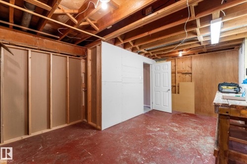 Unfinished basement area featuring exposed ceiling joists and support beams, a partially finished wall with a white paneled door, and concrete flooring - 15112 76A Avenue, Edmonton, AB 