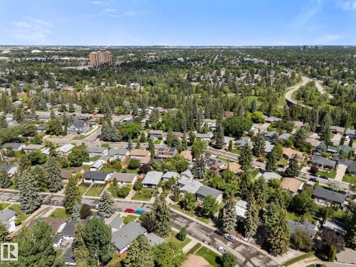 Aerial perspective showcasing a residential neighborhood with extensive tree coverage and a distant urban skyline - 15112 76A Avenue, Edmonton, AB 