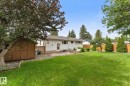 Expansive grassy yard featuring a stone patio, mature trees, wood fence, and a storage shed - 15112 76A Avenue, Edmonton, AB 