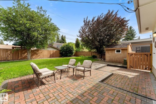 Expansive backyard featuring a brick paver patio, a manicured lawn, a detached storage shed, and mature trees - 15112 76A Avenue, Edmonton, AB 