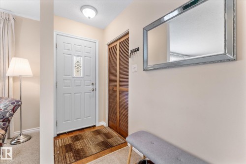 Entryway featuring a white paneled door with decorative glass insert, wood-finish flooring, a flush-mount ceiling light fixture, and a louvered bifold closet door - 15112 76A Avenue, Edmonton, AB 