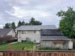 Rear exterior featuring a grey shingle roof, stucco siding, and a spacious green lawn - 