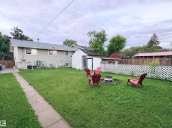 Expansive grass yard featuring a fire pit area, white lattice fencing, and a concrete paver pathway - 