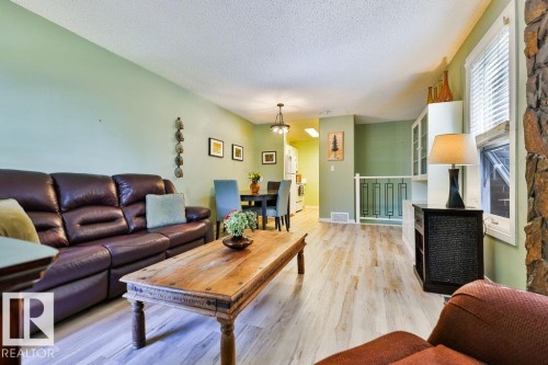 Open-concept living space featuring wood-finish flooring, a contemporary ceiling fixture, a built-in display cabinet with glass doors, and a stone accent wall - 17009 109 Street, Edmonton, AB 