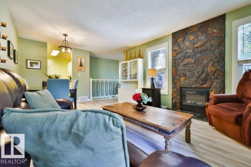 Living area featuring a stone accent wall with a built-in fireplace, light wood-finish flooring, and a decorative white railing - 17009 109 Street, Edmonton, AB 