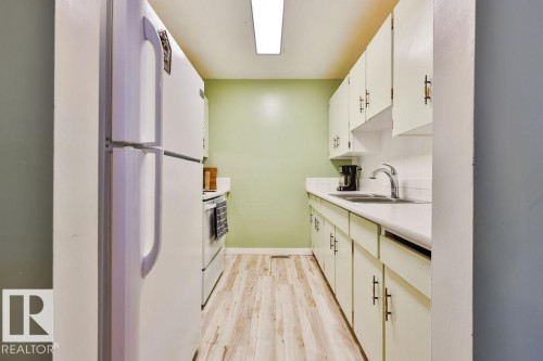 Galley kitchen featuring wood-finish flooring, white cabinetry with dark hardware, a white sink, and white countertops - 17009 109 Street, Edmonton, AB 