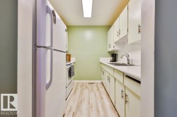 Galley kitchen featuring wood-finish flooring, white cabinetry with dark hardware, a white sink, and white countertops - 