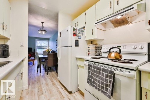 Kitchen featuring white cabinetry with dark hardware, white countertops, a white range with overhead ventilation, and a white refrigerator - 17009 109 Street, Edmonton, AB 