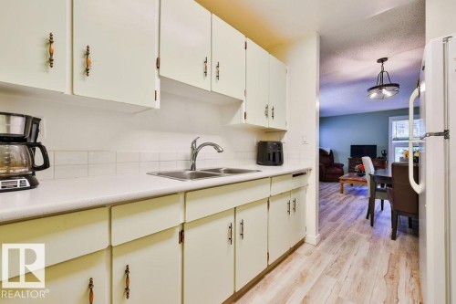 Kitchen featuring light-finish cabinetry with decorative hardware, a double basin stainless steel sink with a chrome faucet, and a white tile backsplash - 17009 109 Street, Edmonton, AB 