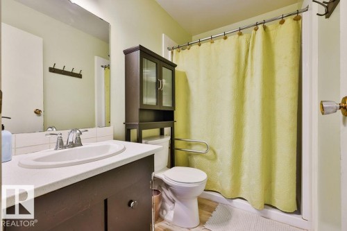 Bathroom featuring a single vanity with a white countertop and chrome faucet, a mounted mirror, and a shower with a privacy curtain - 17009 109 Street, Edmonton, AB 