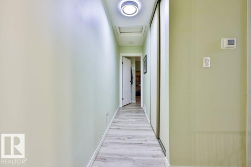 Hallway featuring wood-finish flooring, light green wall paint, and a flush-mount ceiling light - 17009 109 Street, Edmonton, AB 