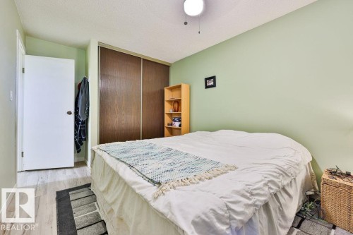Bedroom featuring wood-finish flooring, light green walls, a white door, and sliding closet doors - 17009 109 Street, Edmonton, AB 