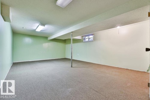 Expansive carpeted room featuring light green and off-white walls, a textured white ceiling, and two fluorescent ceiling light fixtures - 17009 109 Street, Edmonton, AB 