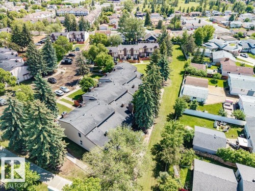 Aerial view showcasing multiple residential buildings with dark shingle roofs, surrounded by mature evergreen trees and green spaces - 17009 109 Street, Edmonton, AB 