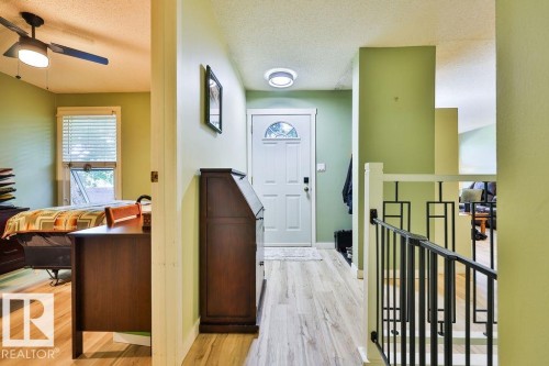 Entryway featuring a white door with an arched decorative glass insert, wood-finish flooring, a contemporary flush-mount ceiling light, and a black metal railing - 17009 109 Street, Edmonton, AB 