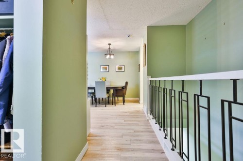 Hallway featuring wood-finish flooring, a modern black metal and white railing, and light green wall paint - 17009 109 Street, Edmonton, AB 