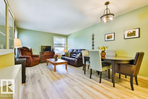 Open concept living area featuring wood-finish flooring, a dining area with an oval table, and a built-in display cabinet - 17009 109 Street, Edmonton, AB 