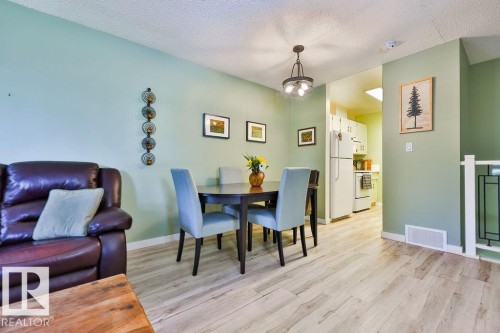 Dining area featuring a contemporary chandelier, light wood-finish flooring, and a partial view of the kitchen with white appliances - 17009 109 Street, Edmonton, AB 