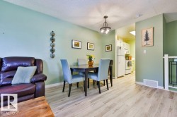 Dining area featuring a contemporary chandelier, light wood-finish flooring, and a partial view of the kitchen with white appliances - 