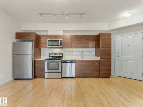 Kitchen featuring wood-finish cabinetry, stainless steel appliances, white countertops, and a white tiled backsplash - 406 9519 160 Avenue, Edmonton, AB 