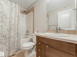 Bathroom featuring a wood-finish vanity with an integrated sink and chrome faucet, a large wall-mounted mirror, and a white bathtub with a shower and tile surround - 
