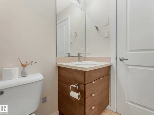 Powder room with a wood-finish vanity, light-colored countertop, and a built-in sink - 406 9519 160 Avenue, Edmonton, AB 