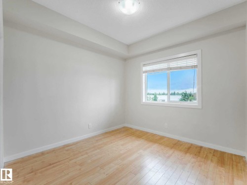 Bright interior space featuring light wood-finish flooring, white baseboards, and a large window with horizontal blinds - 406 9519 160 Avenue, Edmonton, AB 