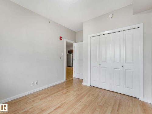 Room featuring wood-finish flooring, light-toned walls, white baseboards, and a double bi-fold closet - 406 9519 160 Avenue, Edmonton, AB 