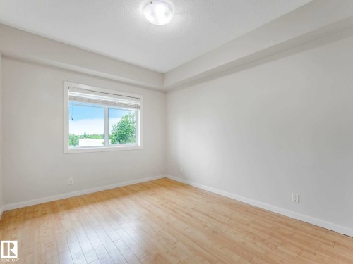 Light-filled room featuring wood-finish flooring, white walls, and a large window - 406 9519 160 Avenue, Edmonton, AB 