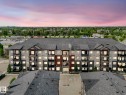 Multi-story residential building with a grey shingle roof and a variety of exterior finishes including light-colored siding, dark grey siding, and red-brown accent panels - 406 9519 160 Avenue, Edmonton, AB 
