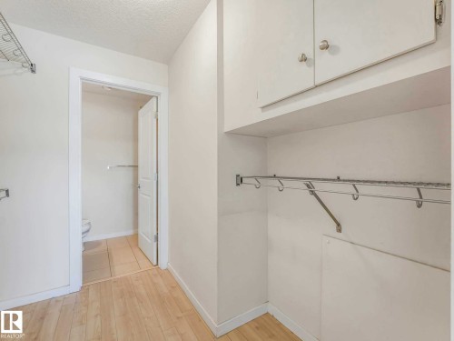 Well-appointed laundry area featuring wood-finish flooring, built-in upper cabinetry, and a wire hanging rack system - 406 9519 160 Avenue, Edmonton, AB 